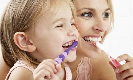 girl brushes teeth with kids toothpaste with her mother